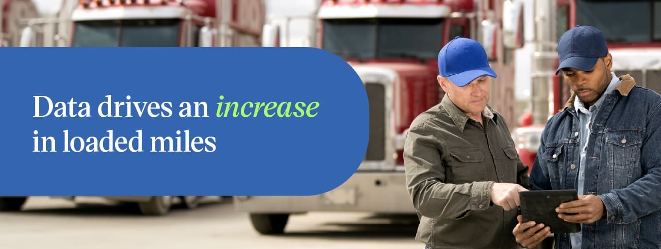 Two fleet workers reviewing data on a tablet near semi trucks